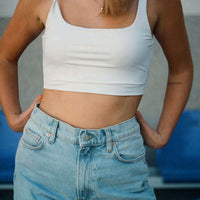 Femme en débardeur blanc et jean, montrant un ventre plat dans un cadre naturel.