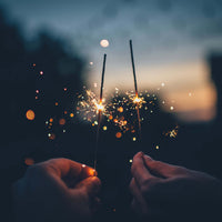 Deux mains tenant des pétards scintillants au crépuscule, symbolisant des résolutions pour la nouvelle année.