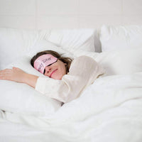 Femme dormant paisiblement avec un masque de sommeil sur des oreillers blancs.