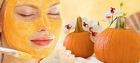 Femme appliquant un masque facial à la citrouille, avec des citrouilles et des fleurs en arrière-plan.